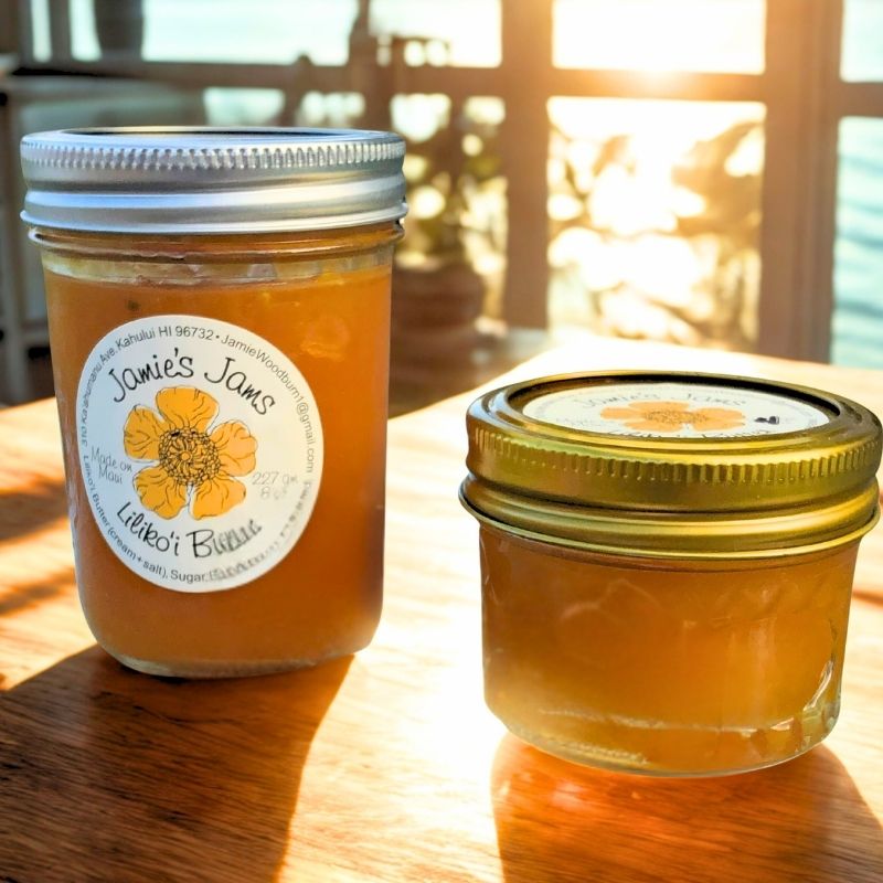 Two jars of lilikoi butter with labels on a wooden surface, sunlit background