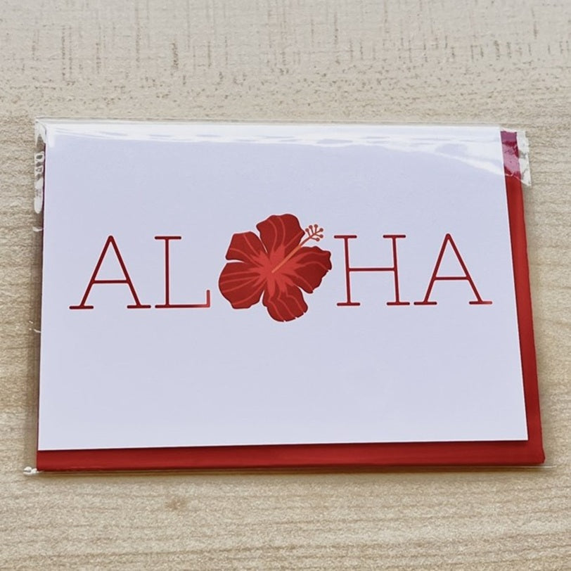 Card with 'ALOHA' and a red flower on a white background, placed on a textured surface.