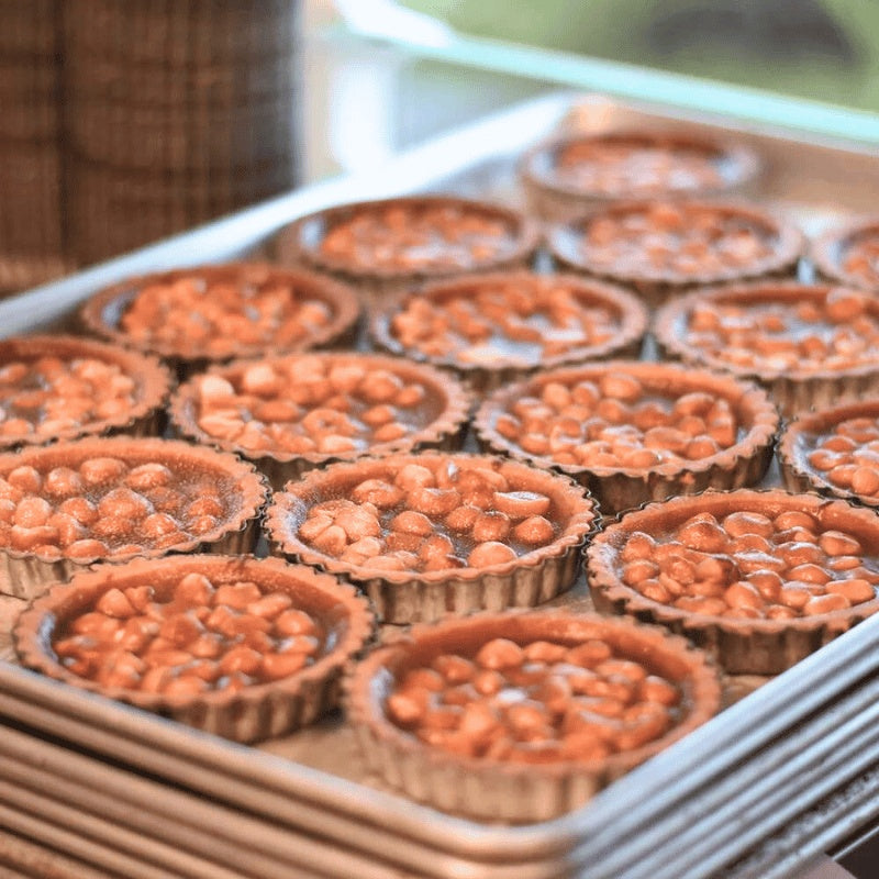 Row of small chocolate tarts with orange toppings on a metal tray.