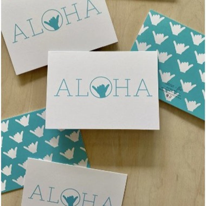 Set of cards with 'ALOHA' text and wave hand symbol on a wooden surface.
