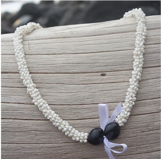 A white lei with black kukui nuts and a purple ribbon tie placed on a wooden surface.